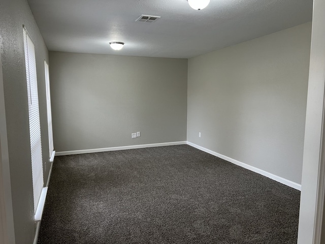 unfurnished room with baseboards, visible vents, dark colored carpet, and a textured ceiling