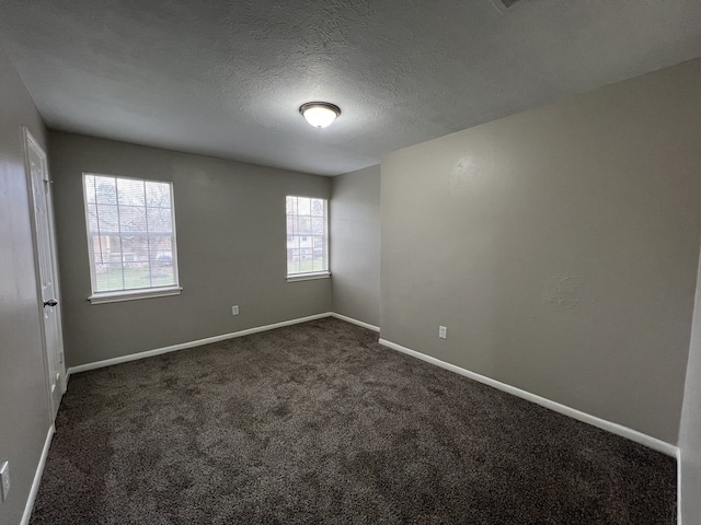 empty room featuring baseboards, dark carpet, and a textured ceiling