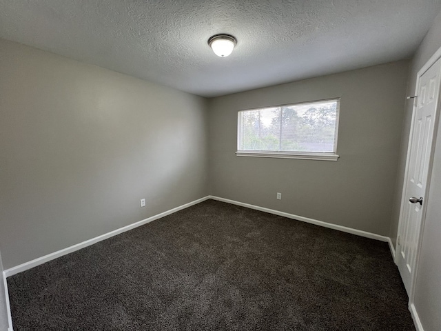 empty room with a textured ceiling, dark colored carpet, and baseboards