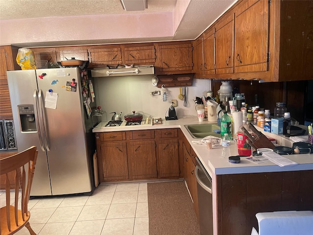 kitchen featuring light tile patterned floors, stainless steel appliances, a sink, light countertops, and brown cabinetry