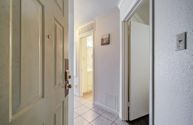 hall featuring light tile patterned floors, a textured ceiling, visible vents, and crown molding