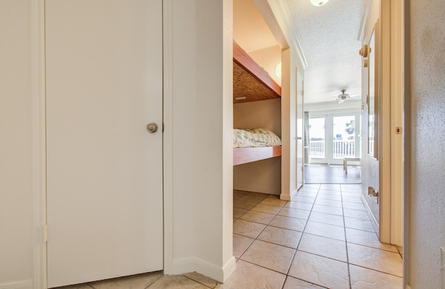 hallway featuring a textured ceiling, light tile patterned floors, and baseboards