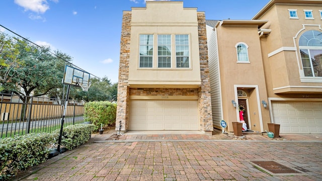 view of property featuring an attached garage, fence, stone siding, decorative driveway, and stucco siding