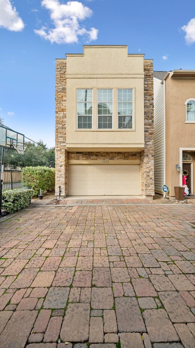 view of front facade featuring a garage, fence, stone siding, decorative driveway, and stucco siding