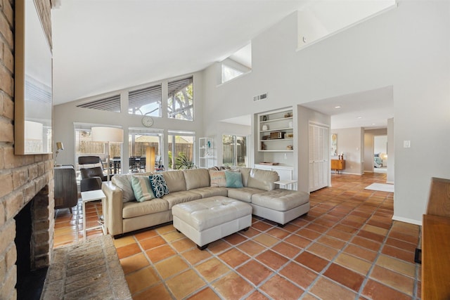 tiled living area with built in shelves, a high ceiling, visible vents, baseboards, and a brick fireplace