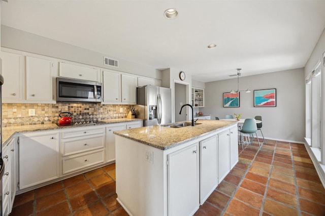 kitchen featuring decorative backsplash, appliances with stainless steel finishes, white cabinets, a kitchen island with sink, and a sink