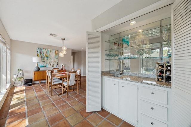 bar with light tile patterned floors, visible vents, decorative light fixtures, a sink, and indoor wet bar