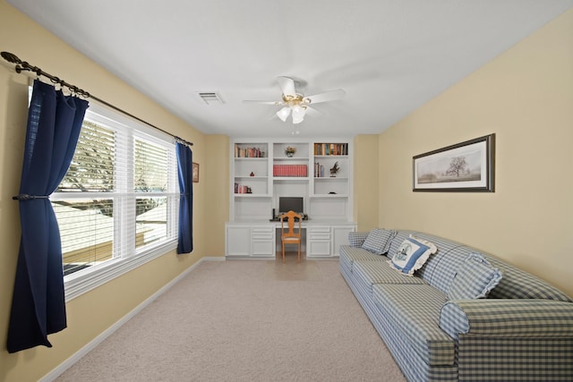 living area with visible vents, a ceiling fan, baseboards, light colored carpet, and built in study area