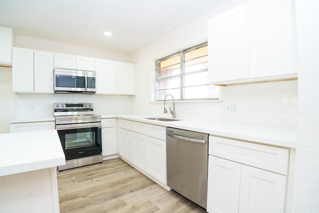 kitchen featuring light wood finished floors, tasteful backsplash, white cabinets, appliances with stainless steel finishes, and a sink