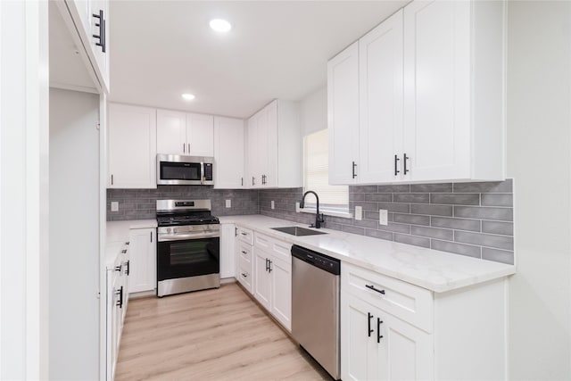 kitchen with light stone counters, stainless steel appliances, a sink, backsplash, and light wood finished floors