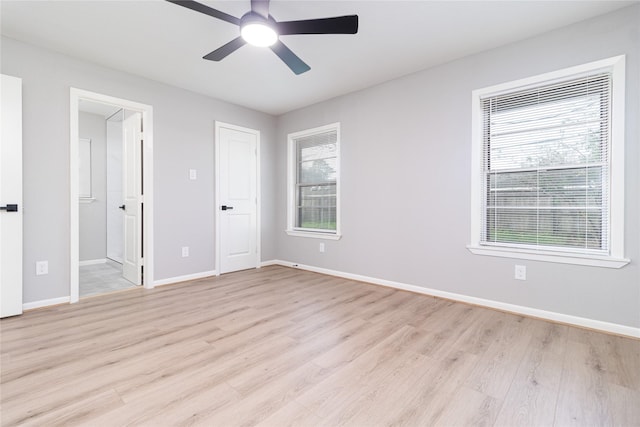 unfurnished bedroom featuring light wood-style floors, ensuite bath, multiple windows, and baseboards