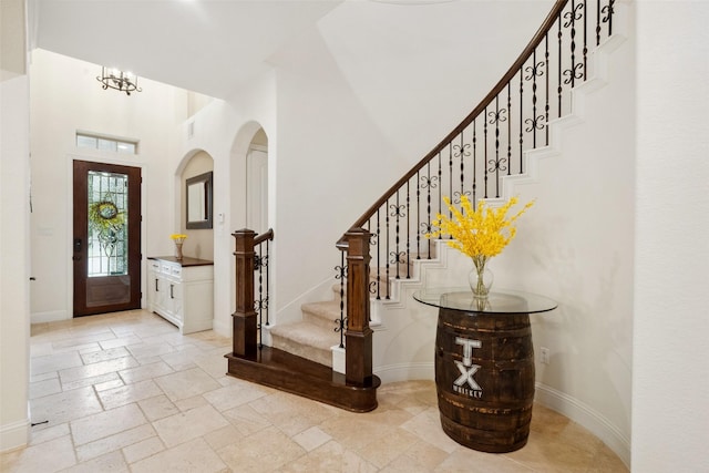 foyer entrance featuring baseboards, stairway, a towering ceiling, and stone tile floors