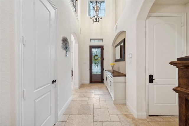 interior space with stone tile floors, baseboards, arched walkways, an inviting chandelier, and a high ceiling