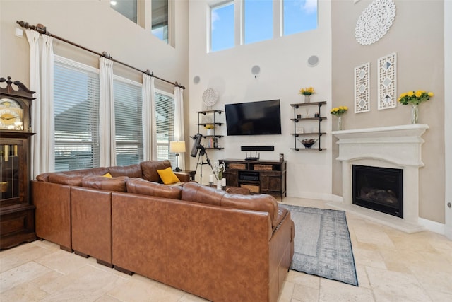 living room featuring a glass covered fireplace, baseboards, a high ceiling, and stone tile floors