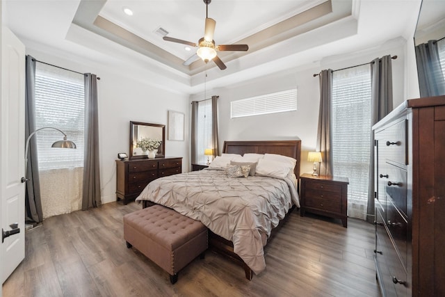 bedroom featuring wood finished floors, visible vents, a ceiling fan, a raised ceiling, and crown molding