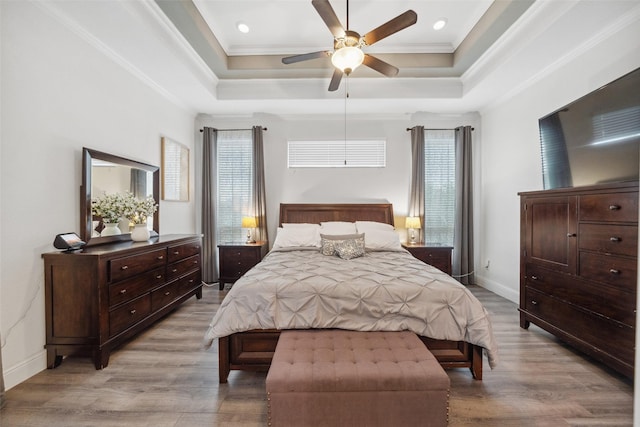 bedroom with light wood-style floors, multiple windows, and a tray ceiling