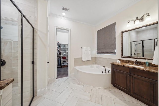 full bathroom featuring visible vents, ornamental molding, a bath, a stall shower, and a walk in closet