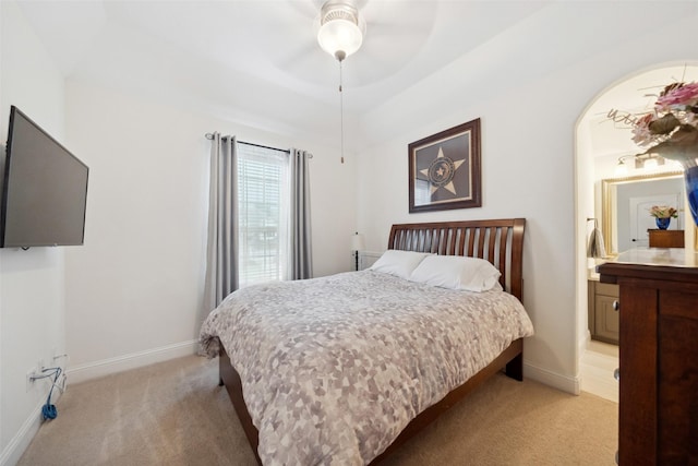 bedroom featuring baseboards, ensuite bath, arched walkways, and light colored carpet