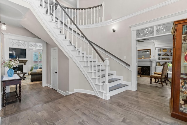 staircase featuring a ceiling fan, a fireplace, baseboards, and wood finished floors