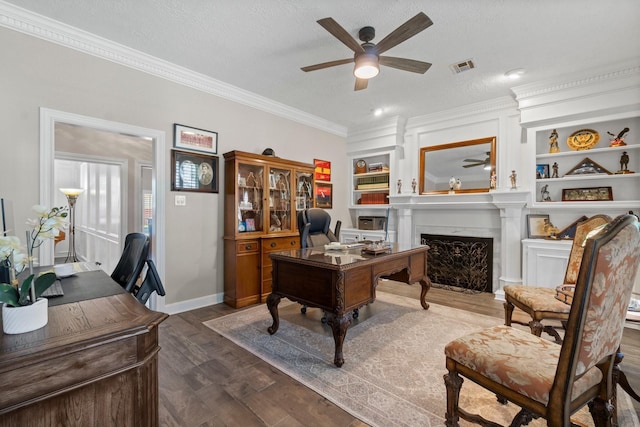 office area with built in shelves, dark wood-style flooring, a fireplace with flush hearth, visible vents, and a ceiling fan