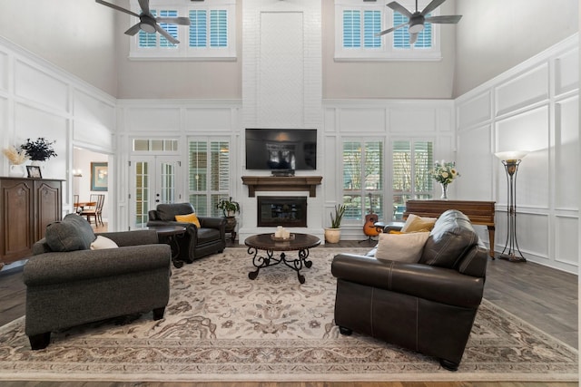 living room with a ceiling fan, a glass covered fireplace, wood finished floors, french doors, and a decorative wall