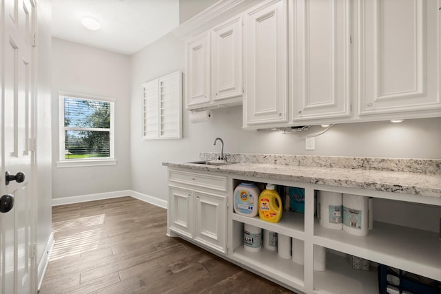 kitchen with dark wood finished floors, white cabinetry, a sink, light stone countertops, and baseboards