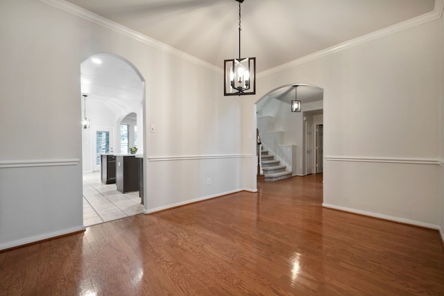 spare room with light wood-type flooring, baseboards, arched walkways, and crown molding