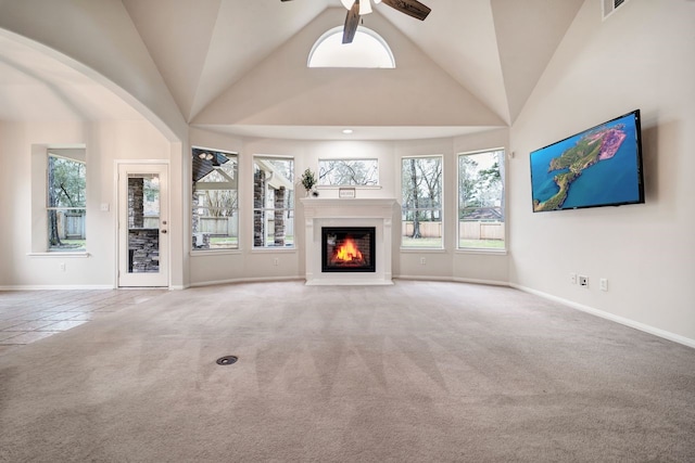 unfurnished living room with high vaulted ceiling, a ceiling fan, baseboards, carpet, and a glass covered fireplace