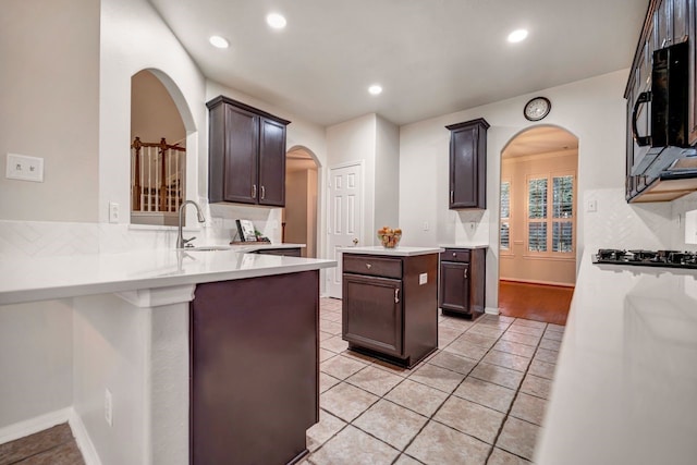 kitchen featuring tasteful backsplash, light countertops, a sink, a peninsula, and black appliances