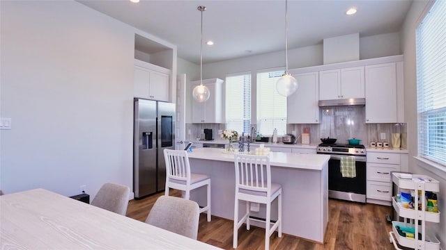 kitchen with under cabinet range hood, stainless steel appliances, white cabinetry, light countertops, and tasteful backsplash