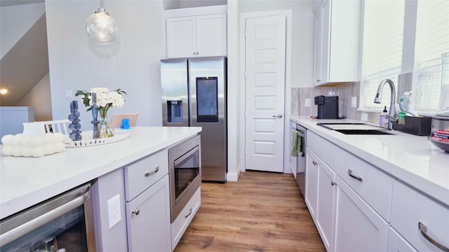 kitchen featuring wine cooler, stainless steel appliances, a sink, white cabinetry, and light countertops