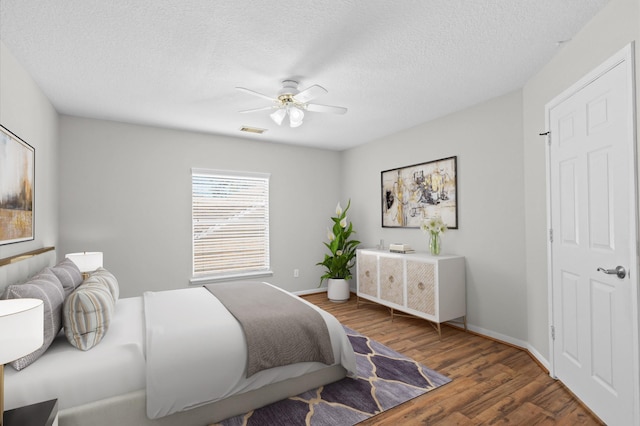 bedroom with ceiling fan, a textured ceiling, baseboards, and wood finished floors