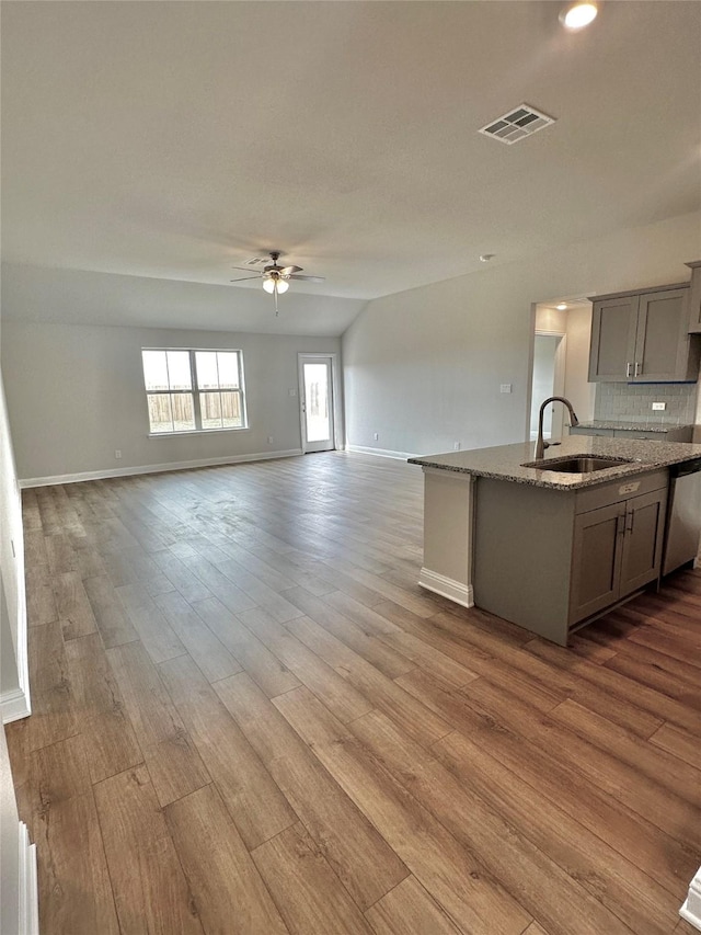 kitchen with light stone counters, wood finished floors, a sink, open floor plan, and decorative backsplash