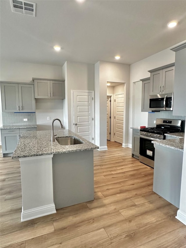 kitchen with stainless steel appliances, visible vents, gray cabinetry, light wood-style floors, and a sink