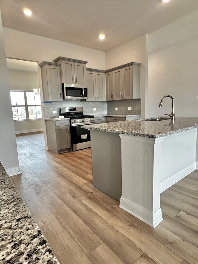 kitchen featuring stainless steel appliances, backsplash, gray cabinetry, light wood-style floors, and a sink