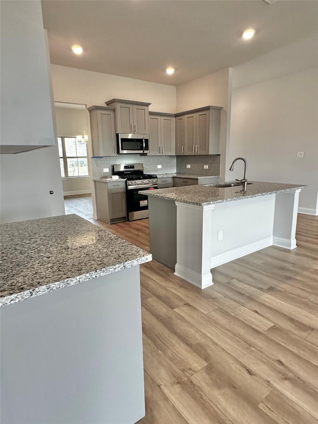 kitchen with appliances with stainless steel finishes, a sink, gray cabinetry, light wood-type flooring, and backsplash