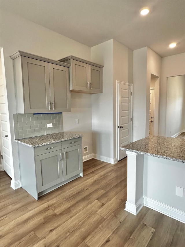 kitchen featuring light wood-type flooring, gray cabinets, decorative backsplash, and light stone countertops