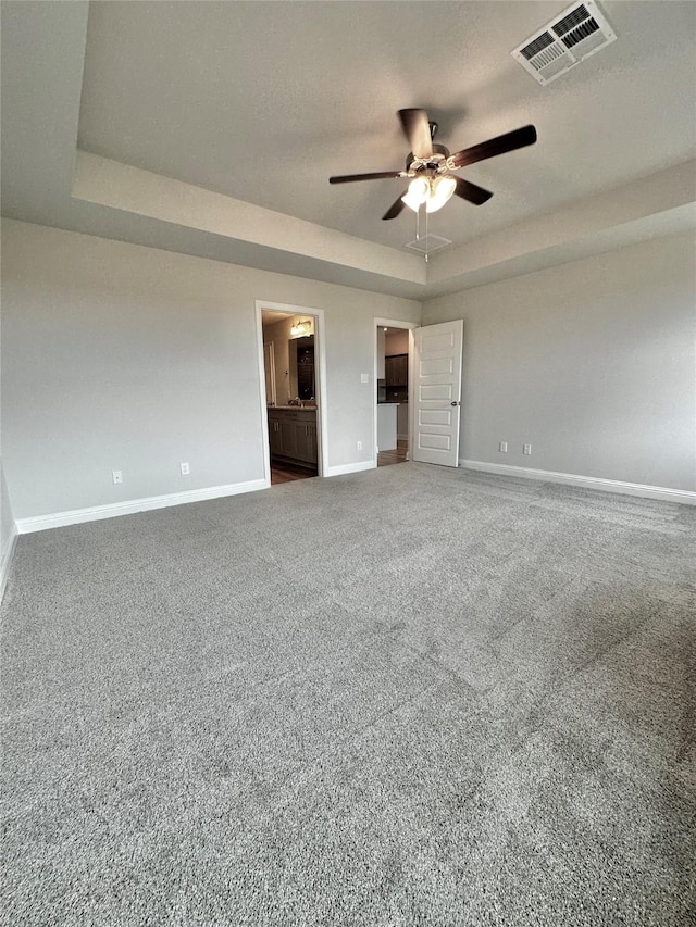 unfurnished bedroom with visible vents, baseboards, connected bathroom, a tray ceiling, and carpet floors