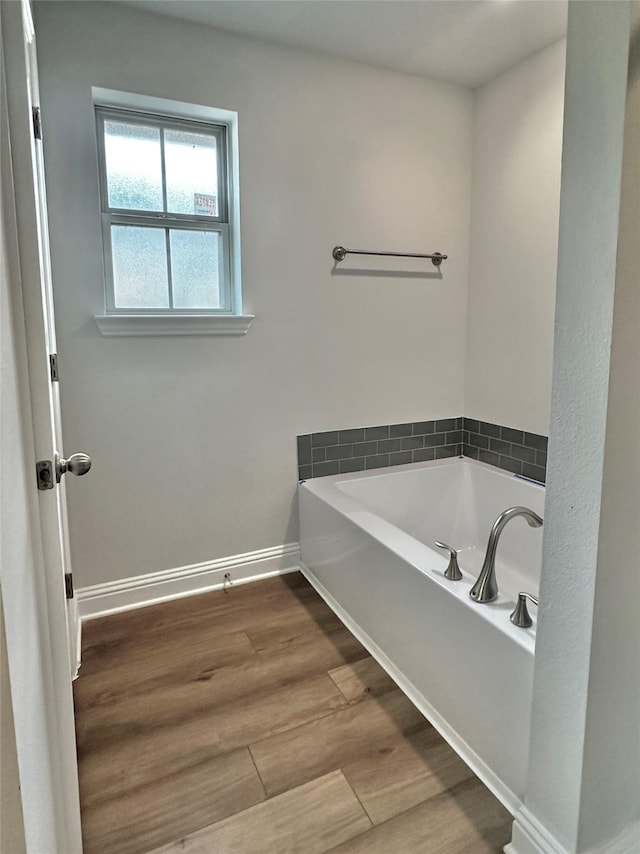 bathroom with a bath, baseboards, and wood finished floors