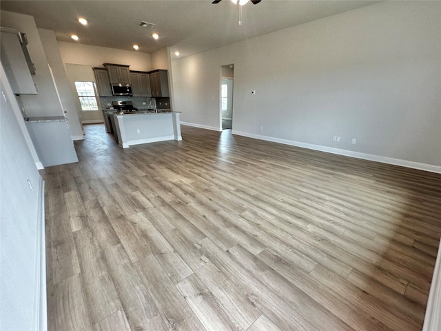 kitchen with stainless steel appliances, open floor plan, ceiling fan, wood finished floors, and baseboards