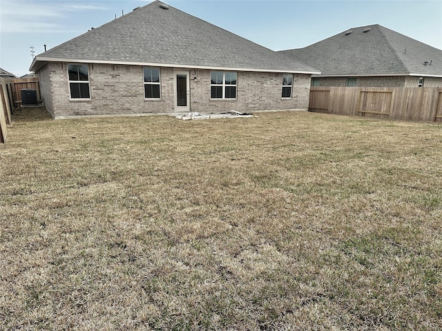 rear view of house featuring a fenced backyard, central AC, brick siding, a lawn, and roof with shingles