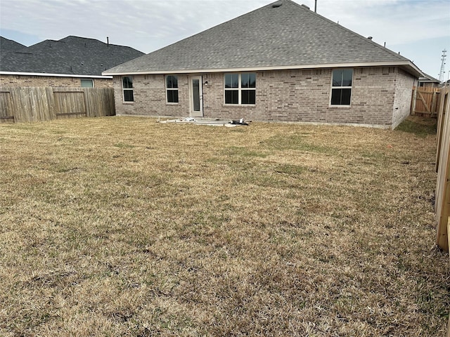 rear view of property with brick siding, a fenced backyard, a shingled roof, and a yard