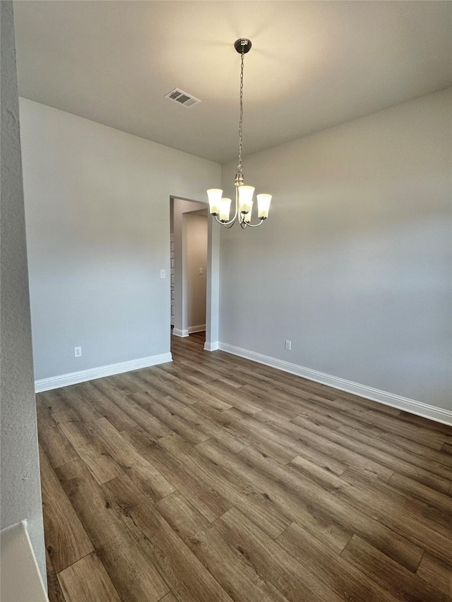 unfurnished room with dark wood-type flooring, visible vents, baseboards, and an inviting chandelier