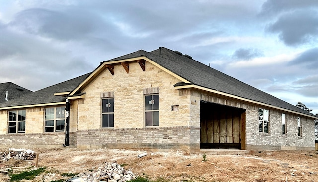 view of side of property with brick siding, stone siding, and a shingled roof