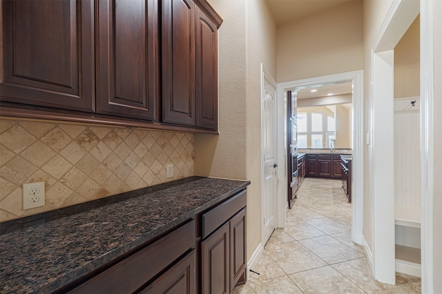 23403 Clark Arbor Ln, Katy, TX 77493 - kitchen featuring light tile patterned floors, stainless steel oven, dark brown cabinets, backsplash, and dark stone countertops