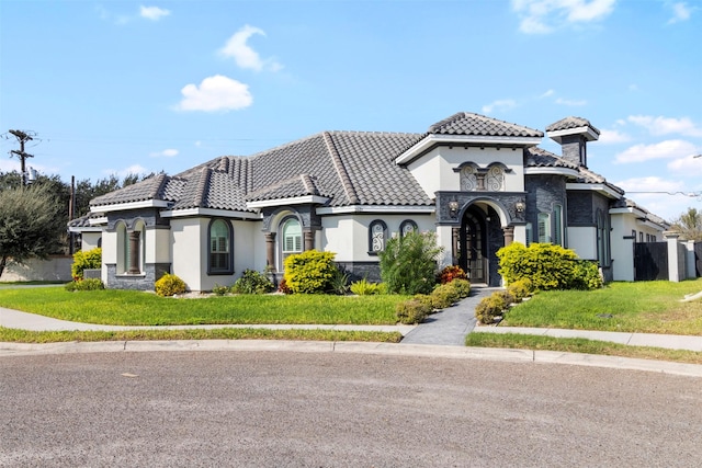 mediterranean / spanish home featuring a tiled roof, a front lawn, stone siding, and stucco siding