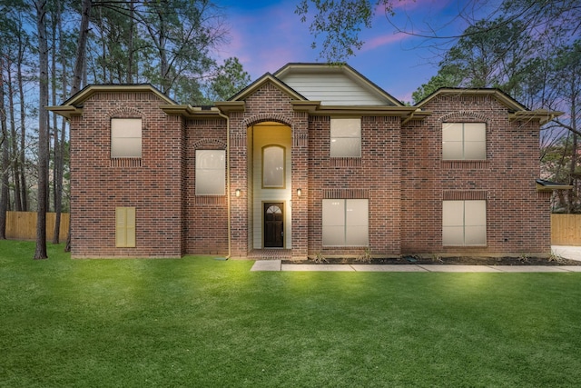 view of front of property featuring brick siding, fence, and a front lawn