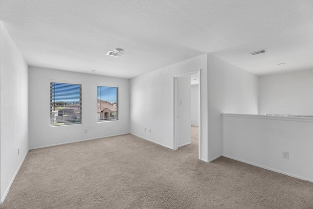 spare room with carpet, a textured ceiling, visible vents, and baseboards