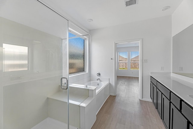 bathroom with a stall shower, visible vents, wood finished floors, a garden tub, and vanity