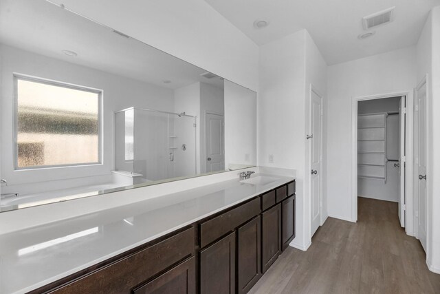 bathroom featuring wood finished floors, vanity, visible vents, a spacious closet, and walk in shower